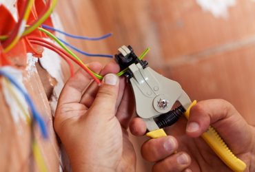 Electrician peeling off insulation from wires - closeup on hands and pliers